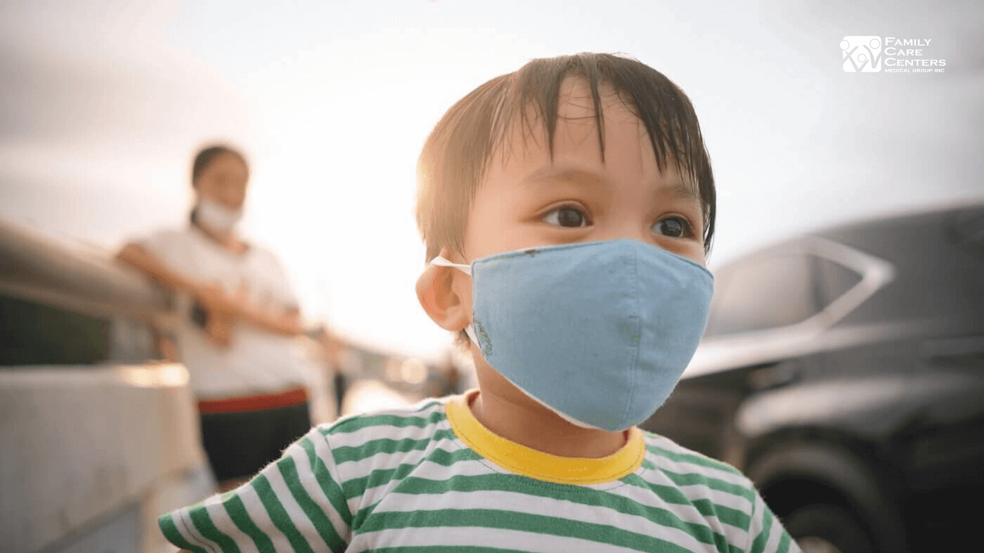 Kid with face mask playing and mother watching from behind